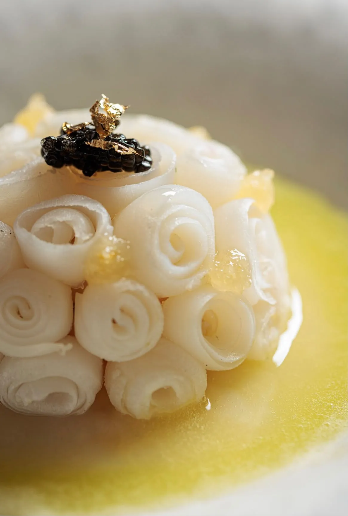 Cupola di rotolini di pesce crudo con caviale nero e foglia d'oro su crema chiara